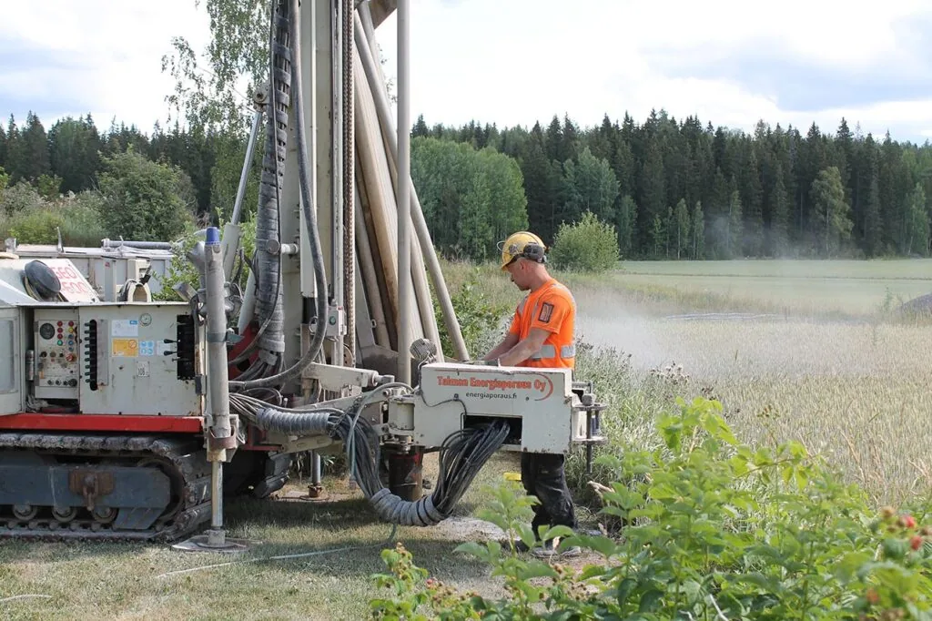 Energiaporauskalusto poraamassa lämpökaivoa pellon laidalla, asentaja ohjaamassa poraa.
